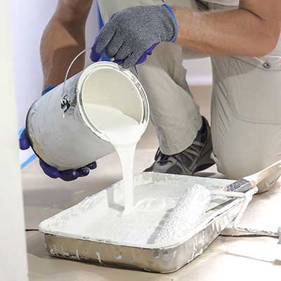 Close up of a worker pouring white paint into a paint roller tray